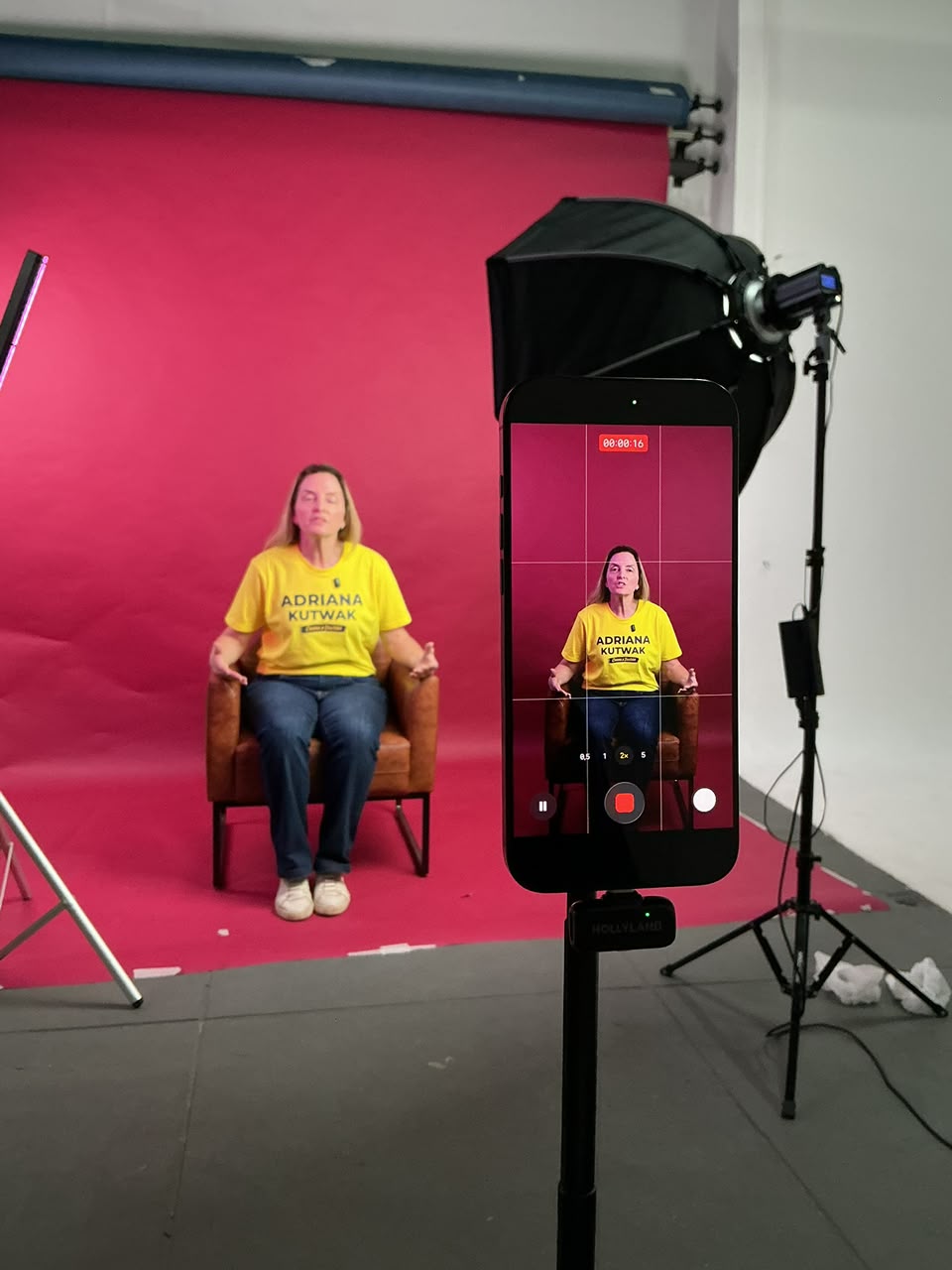 Gravação em estúdio: cliente sentada diante de fundo colorido, iluminada por softbox e enquadrada no celular